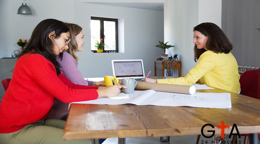 Architects working with drawings at desk in office. Three women discussing house design with office interior in background. House design and architecture concept.