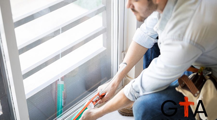 Closeup of a young handyman applying some sealant on a door with a sealing gun
