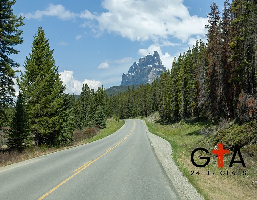 An empty road in the middle of a forest with the Castle Mountain in the distance in Alberta Canada