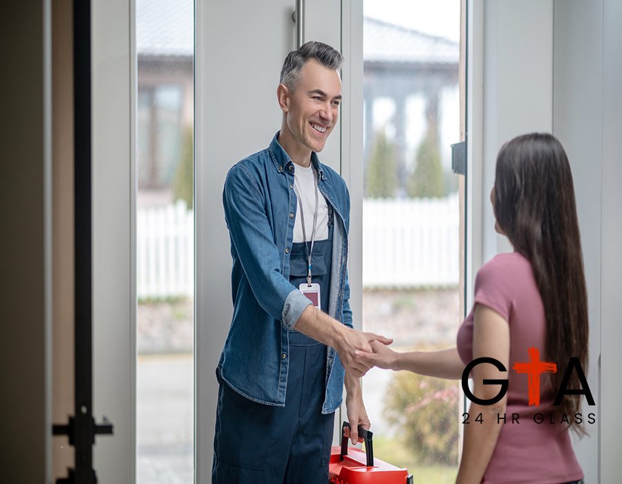 Greetings. Joyful man in blue overalls with badge on neck and woman with long dark hair standing with back to camera shaking hands near glass door indoors