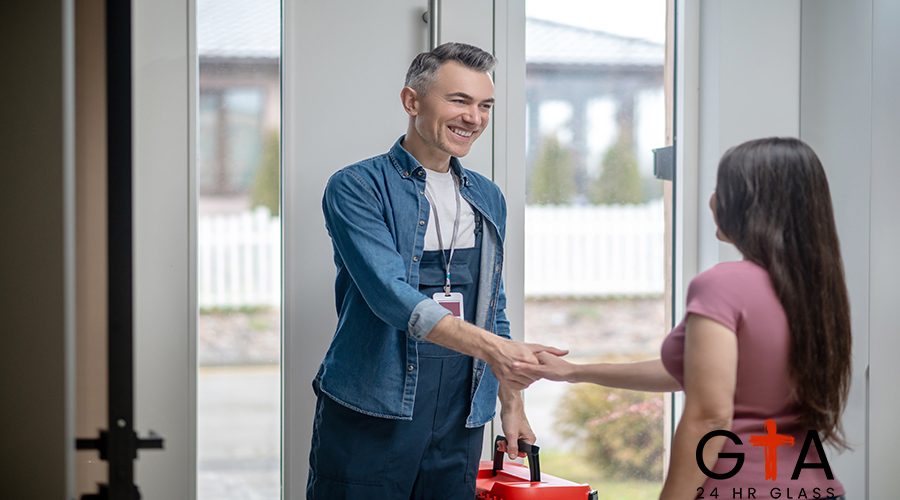 Greetings. Joyful man in blue overalls with badge on neck and woman with long dark hair standing with back to camera shaking hands near glass door indoors