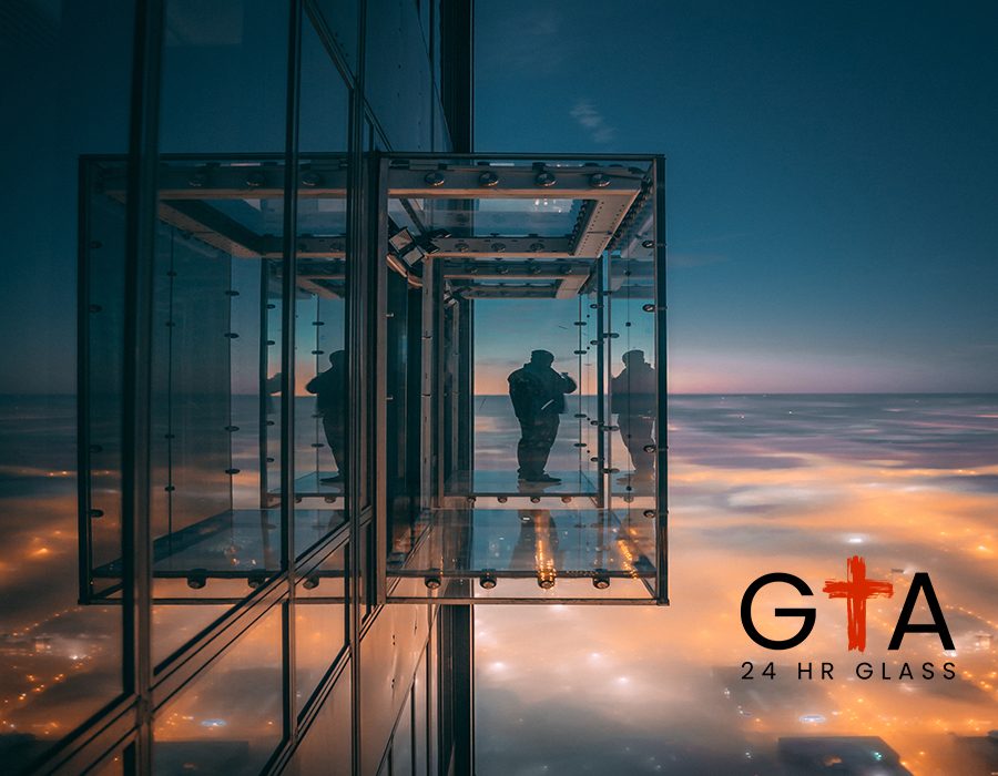 A person standing and enjoying the beautiful view of the city on a balcony with glass walls in a tall skyscraper