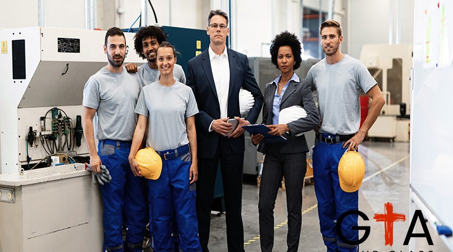 Portrait of group of engineers and corporate managers standing in a factory and looking at camera.