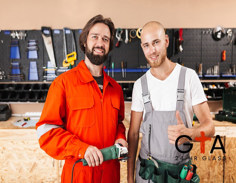 Two smiling builders in work clothes happily looking in camera spending time in workshop with variety of tools on background