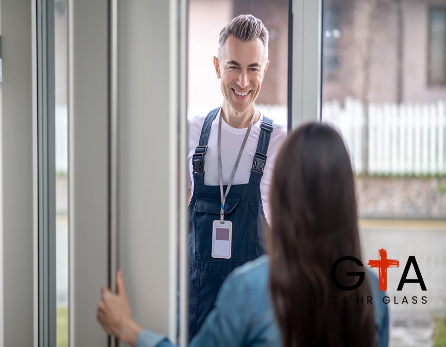 Plumber visit. Dark-haired woman with back to camera at home opening glass door to smiling middle-aged man in white tshirt and blue jumpsuit